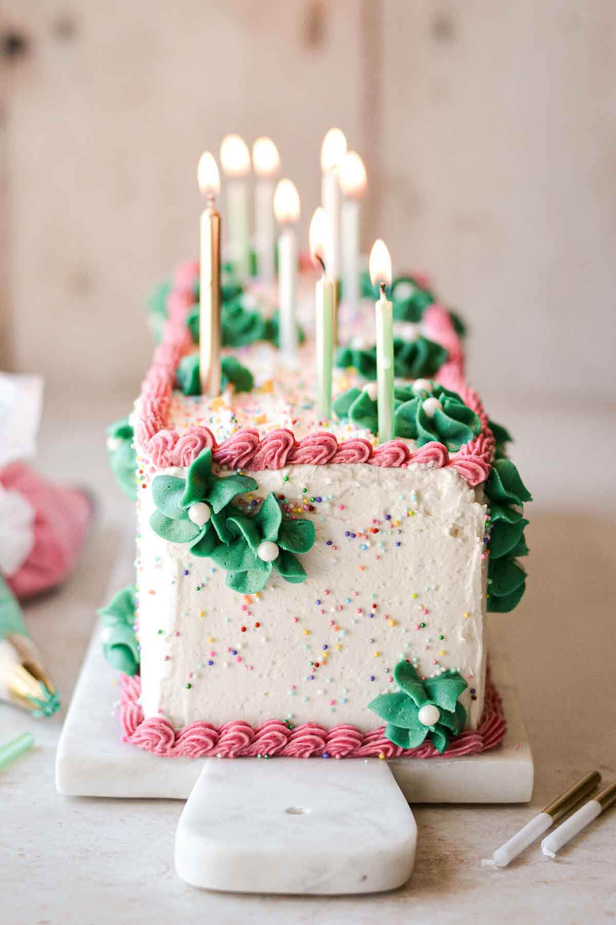 Table runner birthday cake with sprinkles, pink and green buttercream, and birthday candles.