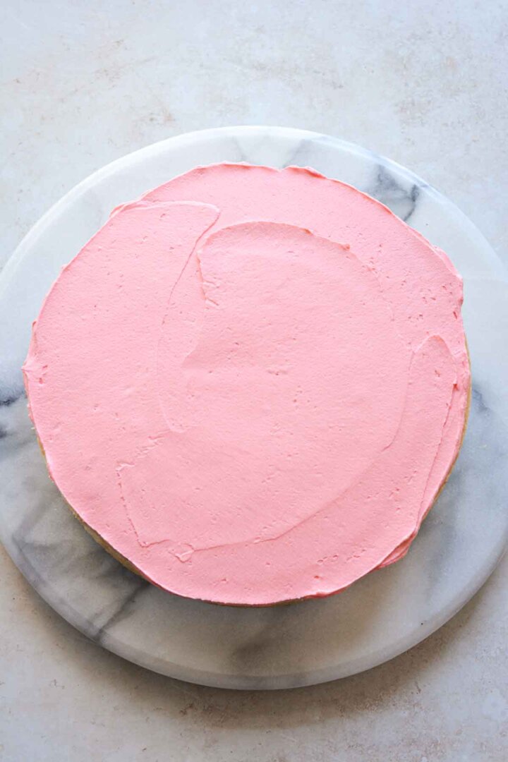 Step 2 for assembling a sugar cookie sprinkle cake - layer of pink buttercream.
