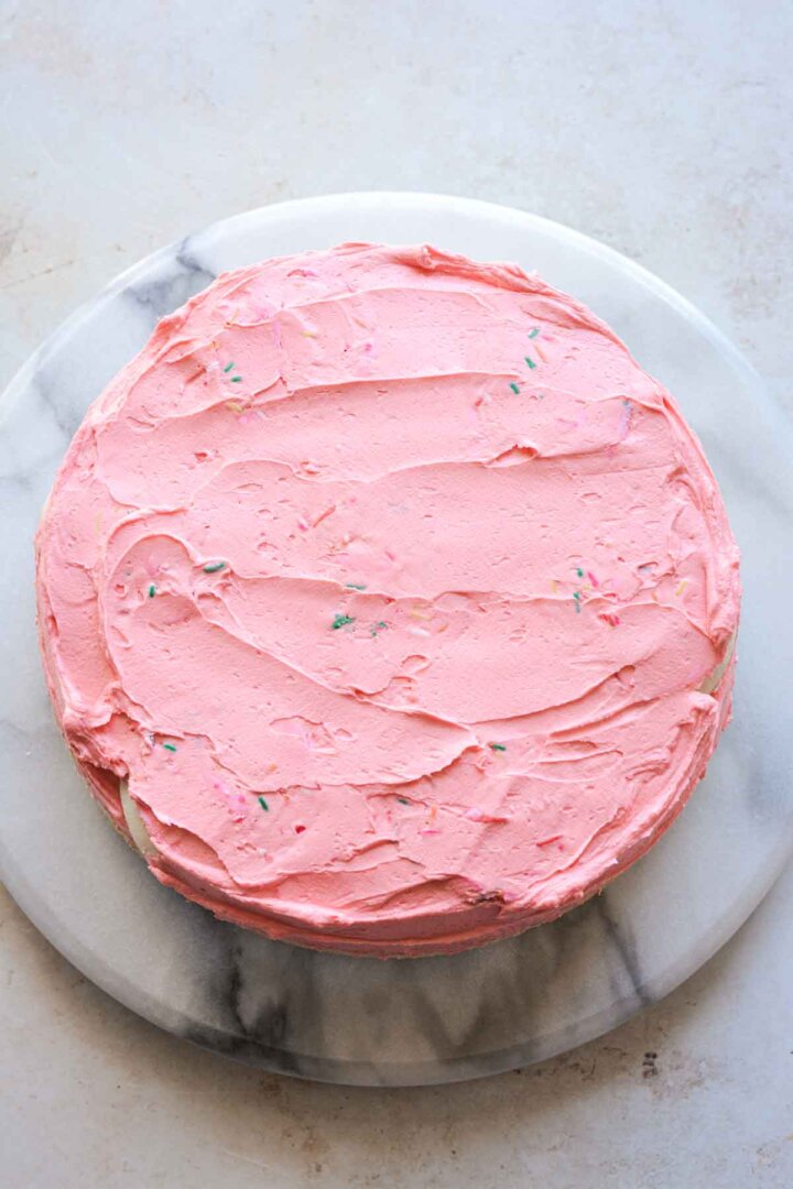 Step 4 for assembling a sugar cookie sprinkle cake - layer of pink buttercream over cookies.