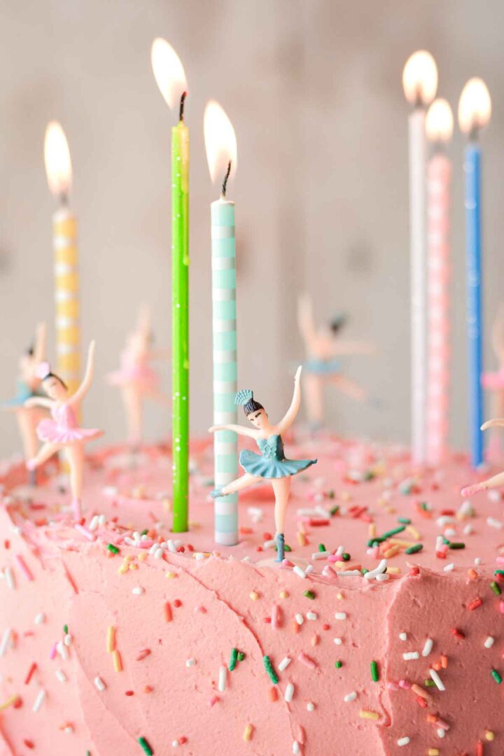 Birthday candles and ballerinas on a pink frosted cake with sprinkles.