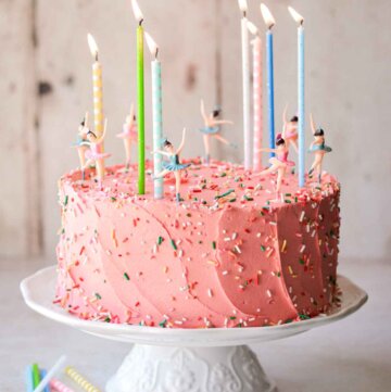 Sugar cookie sprinkle cake on a white cake stand, with colorful birthday candles and dancing ballerinas.