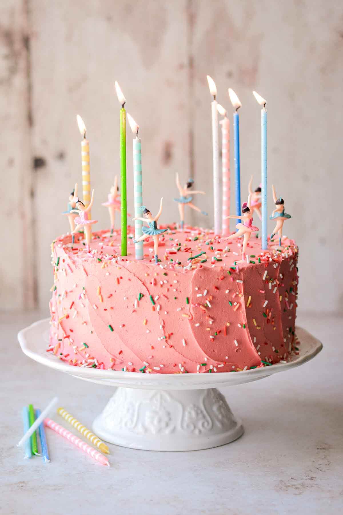 Sugar cookie sprinkle cake on a white cake stand, with colorful birthday candles and dancing ballerinas.