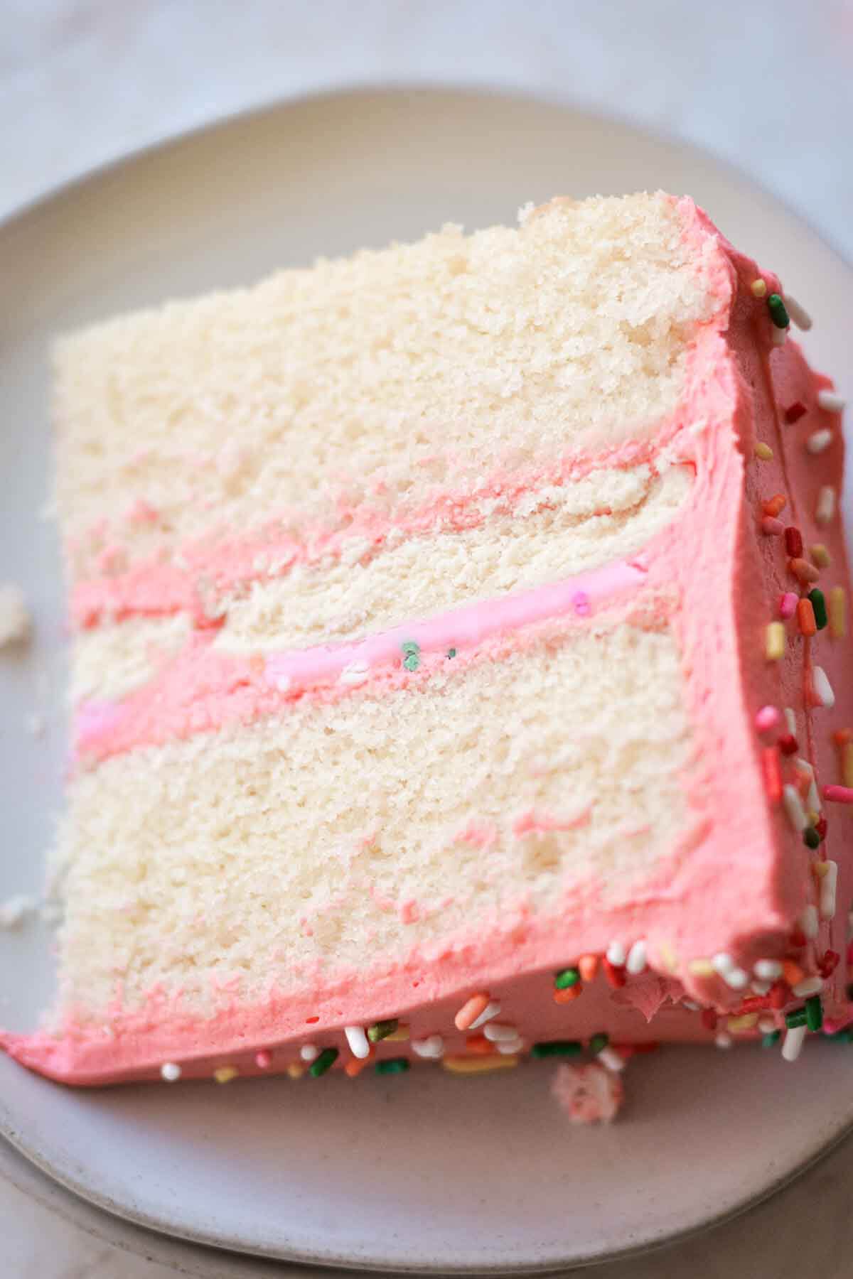 Slice of sugar cookie sprinkle cake with pink frosting.