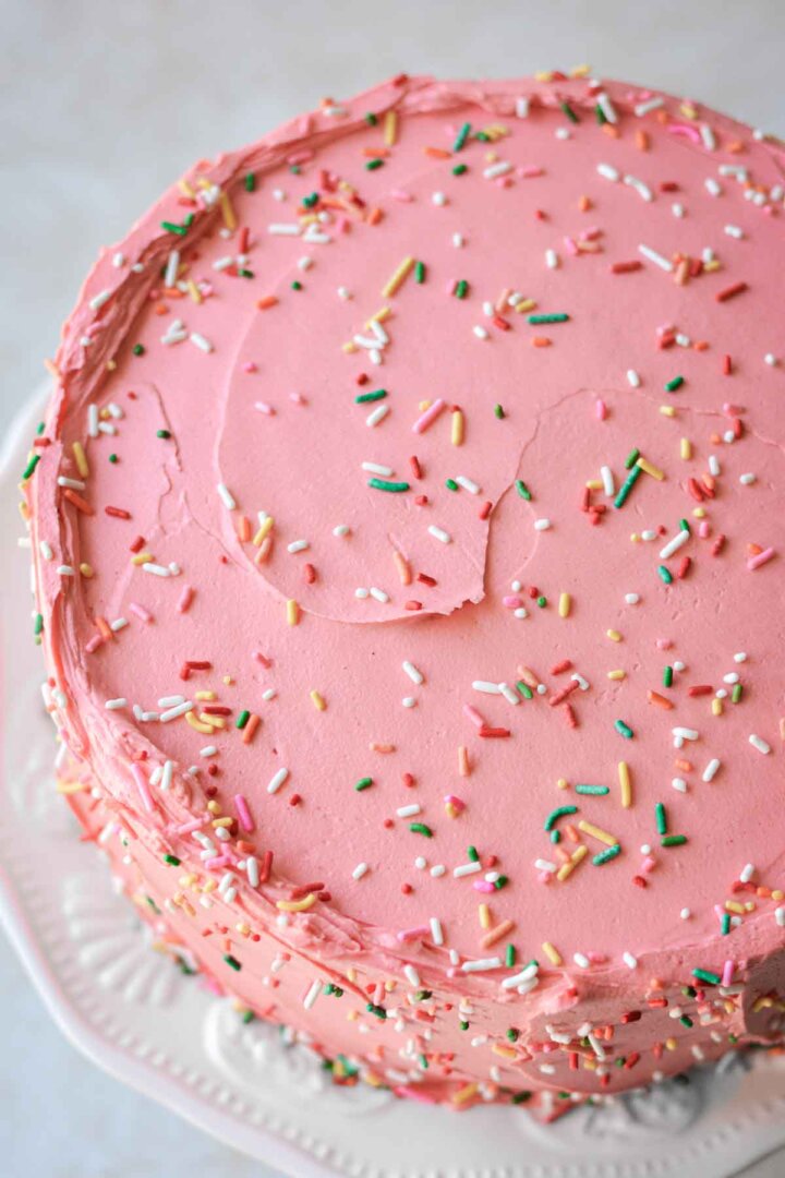 Rainbow sprinkles scattered over a pink frosted birthday cake.