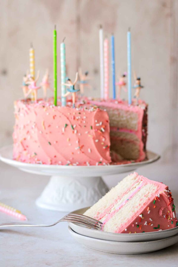 Pink sugar cookie sprinkle cake with one slice cut.