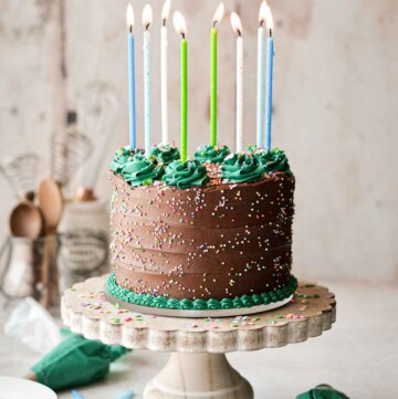 Gluten free chocolate birthday cake with sprinkles, birthday candles, and decorative green buttercream piping.
