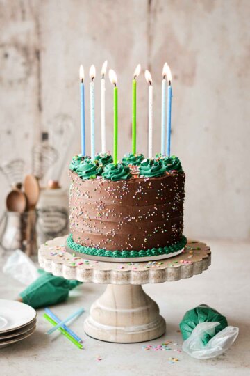 Gluten free chocolate birthday cake with sprinkles, birthday candles, and decorative green buttercream piping.