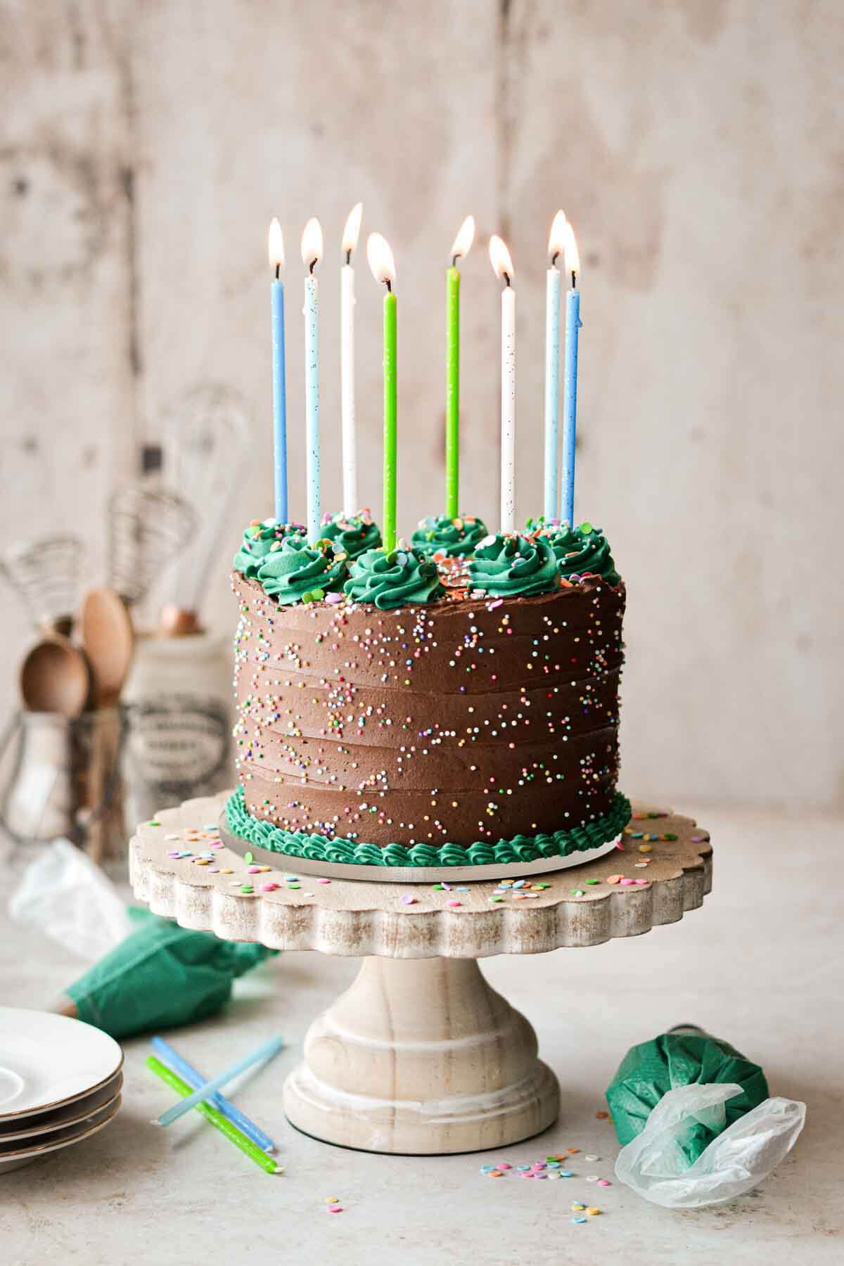 Gluten free chocolate birthday cake with sprinkles, birthday candles, and decorative green buttercream piping.