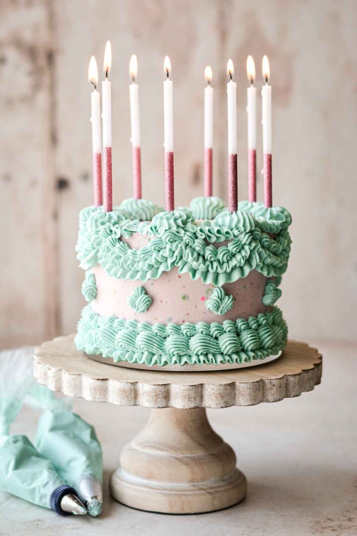Pink and blue Lambeth cake with elaborately piped buttercream and pink birthday candles.