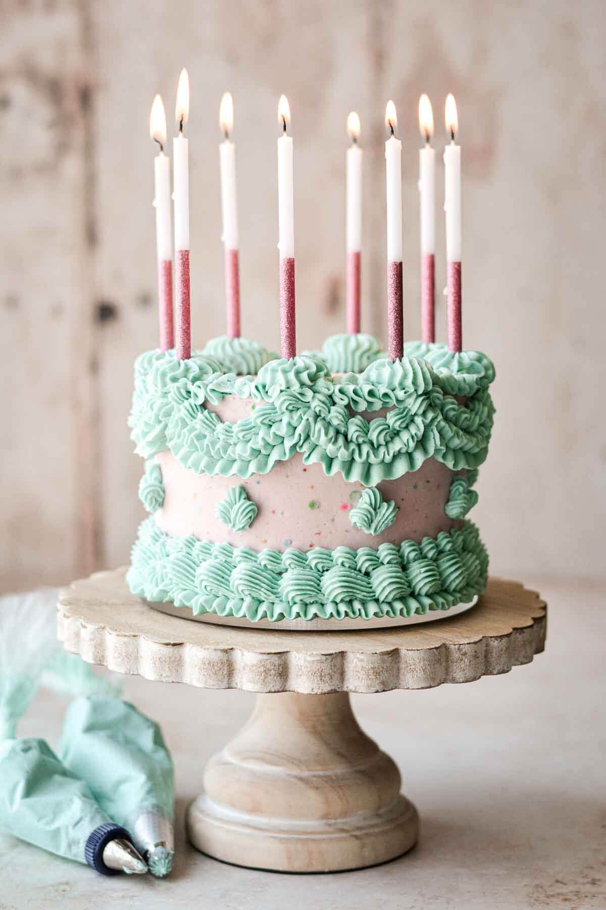 Pink and blue Lambeth cake with elaborately piped buttercream and pink birthday candles.