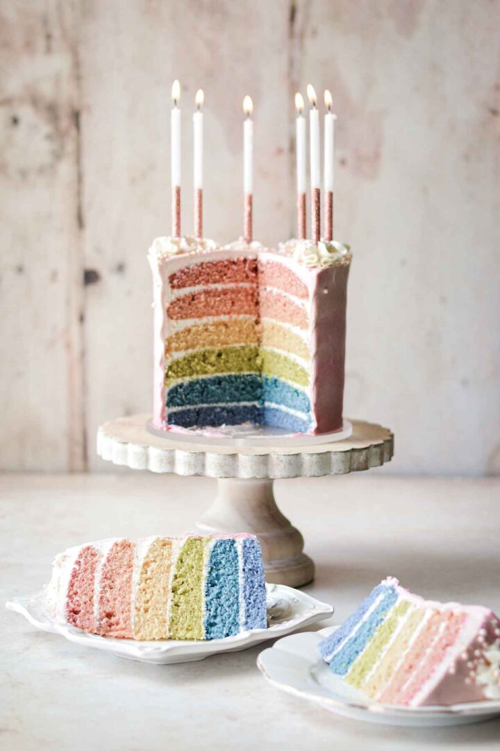 Six-layer rainbow cake with slices of cake on plates.