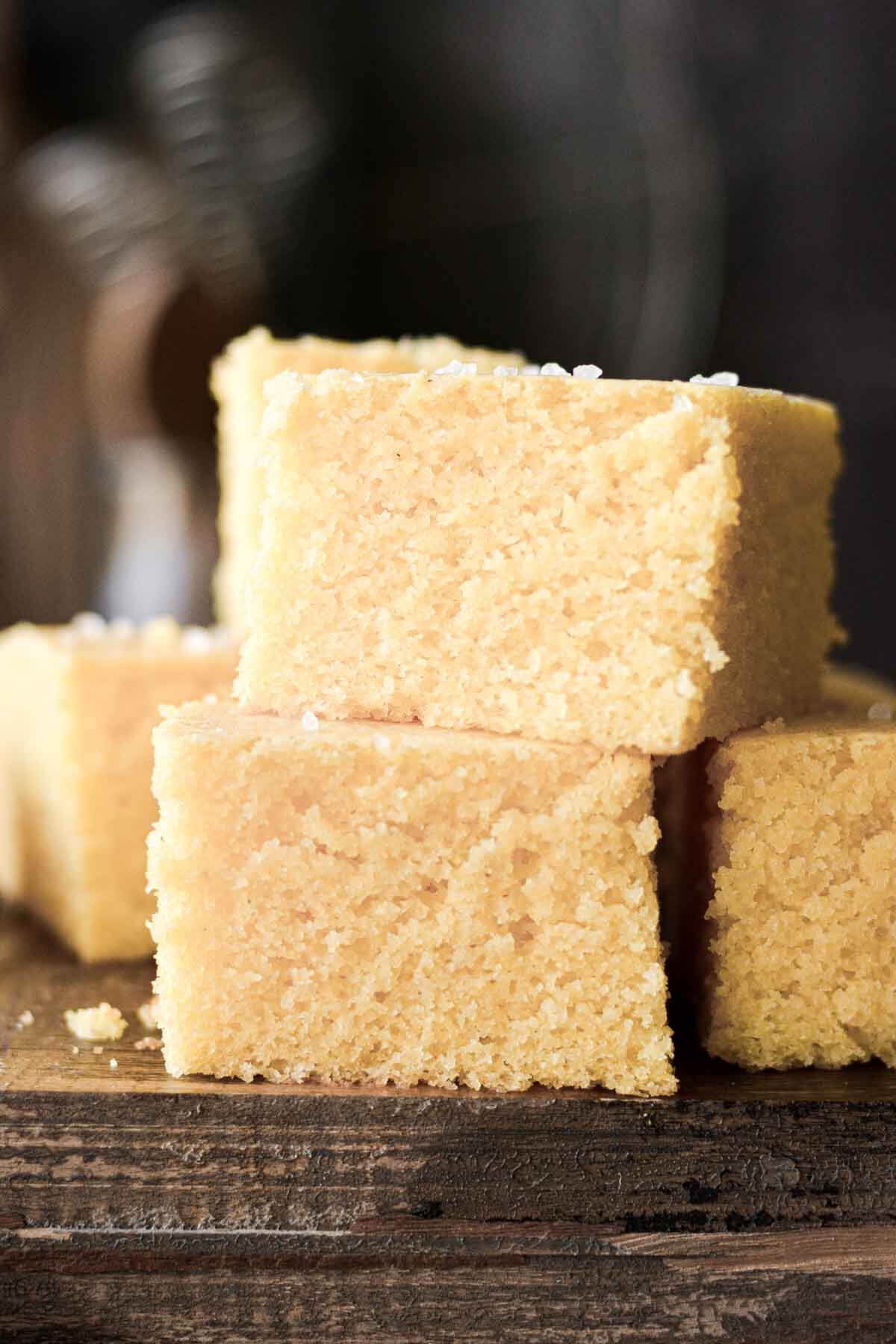 Squares of corn bread stacked on a wooden board.