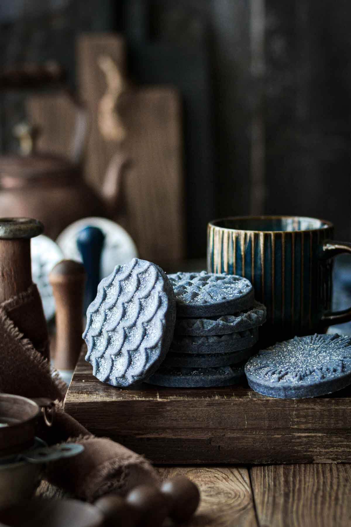 Blue shortbread cookies, stacked on a wooden board.