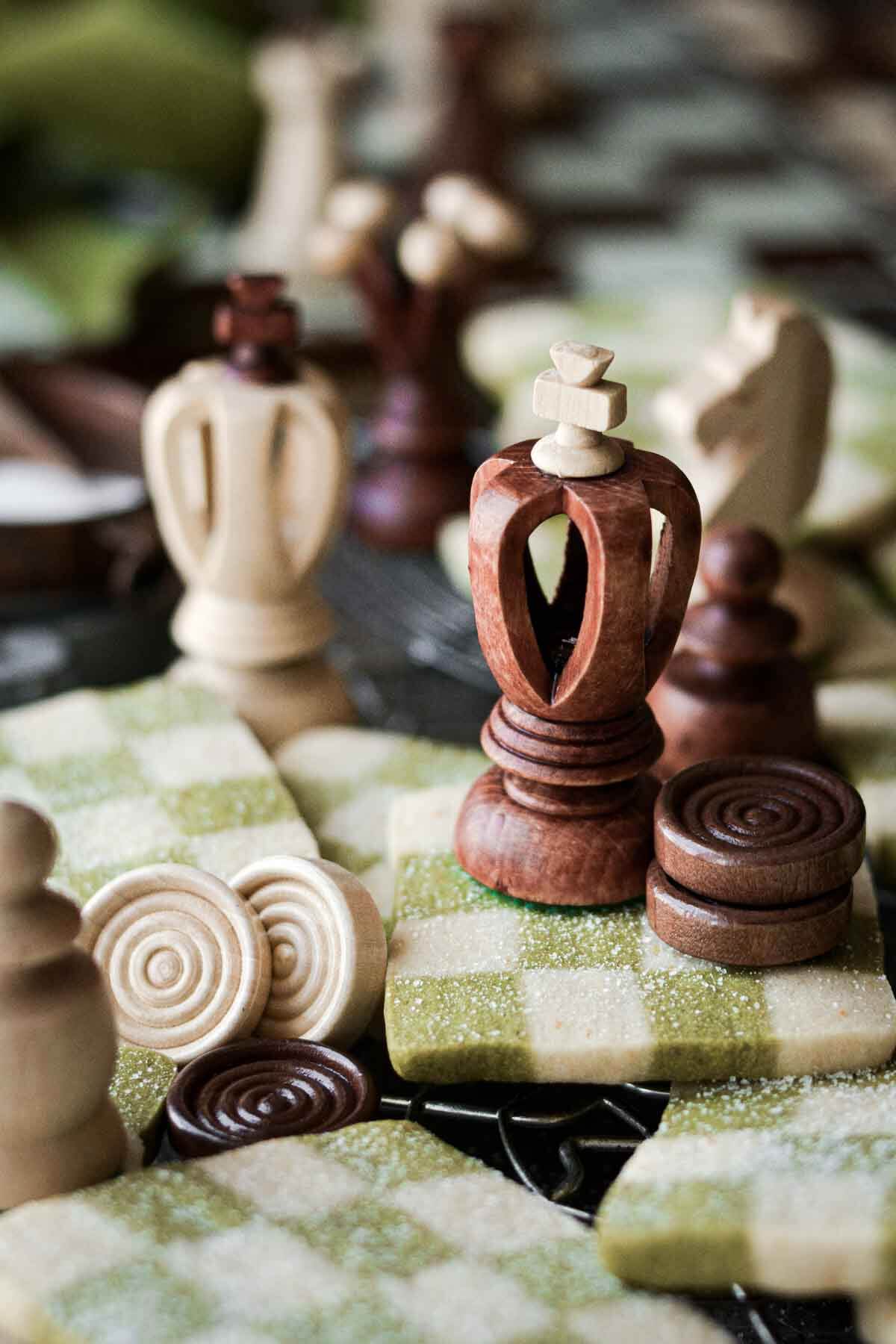 Chess pieces sitting on green and white checkerboard cookies.