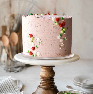 Strawberry matcha cake decorated with a summery strawberry sprinkle mix, on a wooden cake stand.