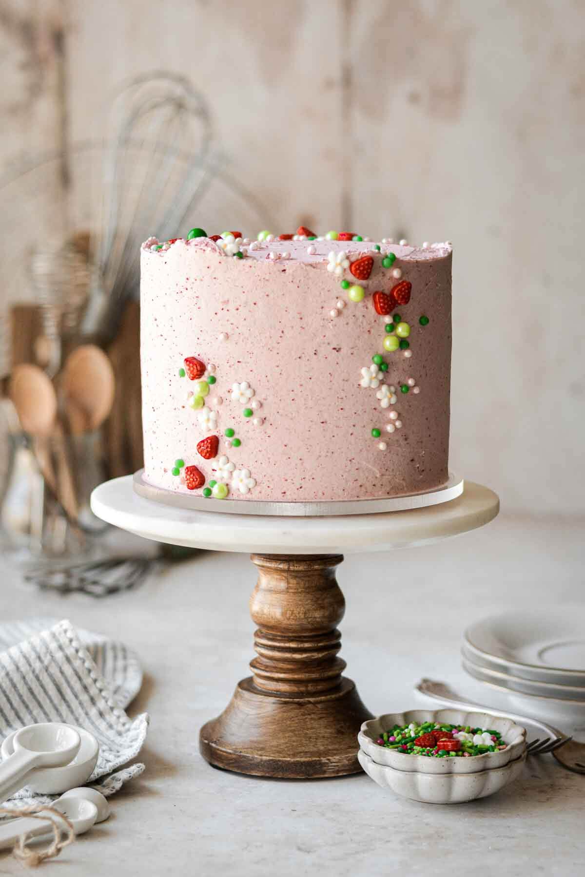 Strawberry matcha cake decorated with a summery strawberry sprinkle mix, on a wooden cake stand.