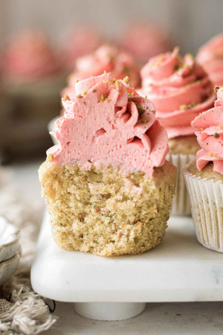 Pistachio cupcake with strawberry frosting, with a bite taken.