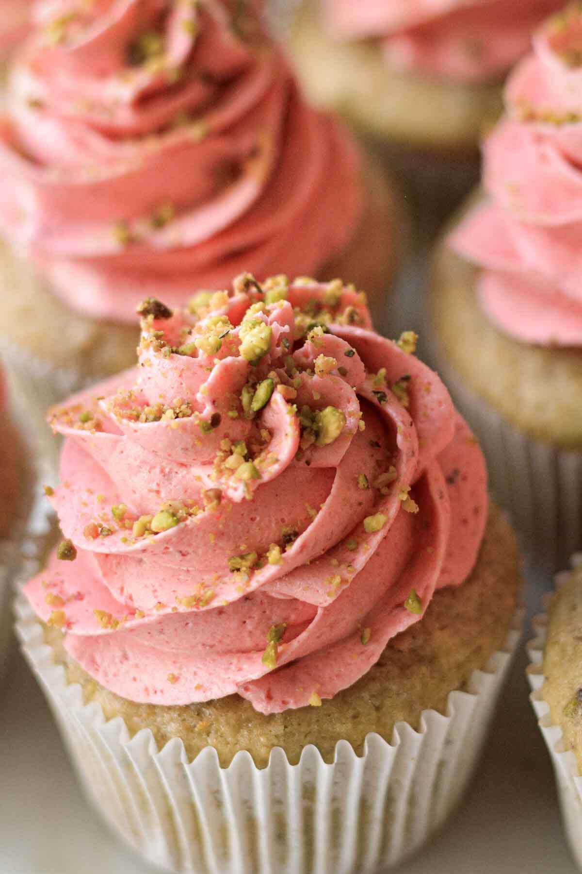 Pistachio cupcakes with strawberry buttercream and crushed pistachios on top.
