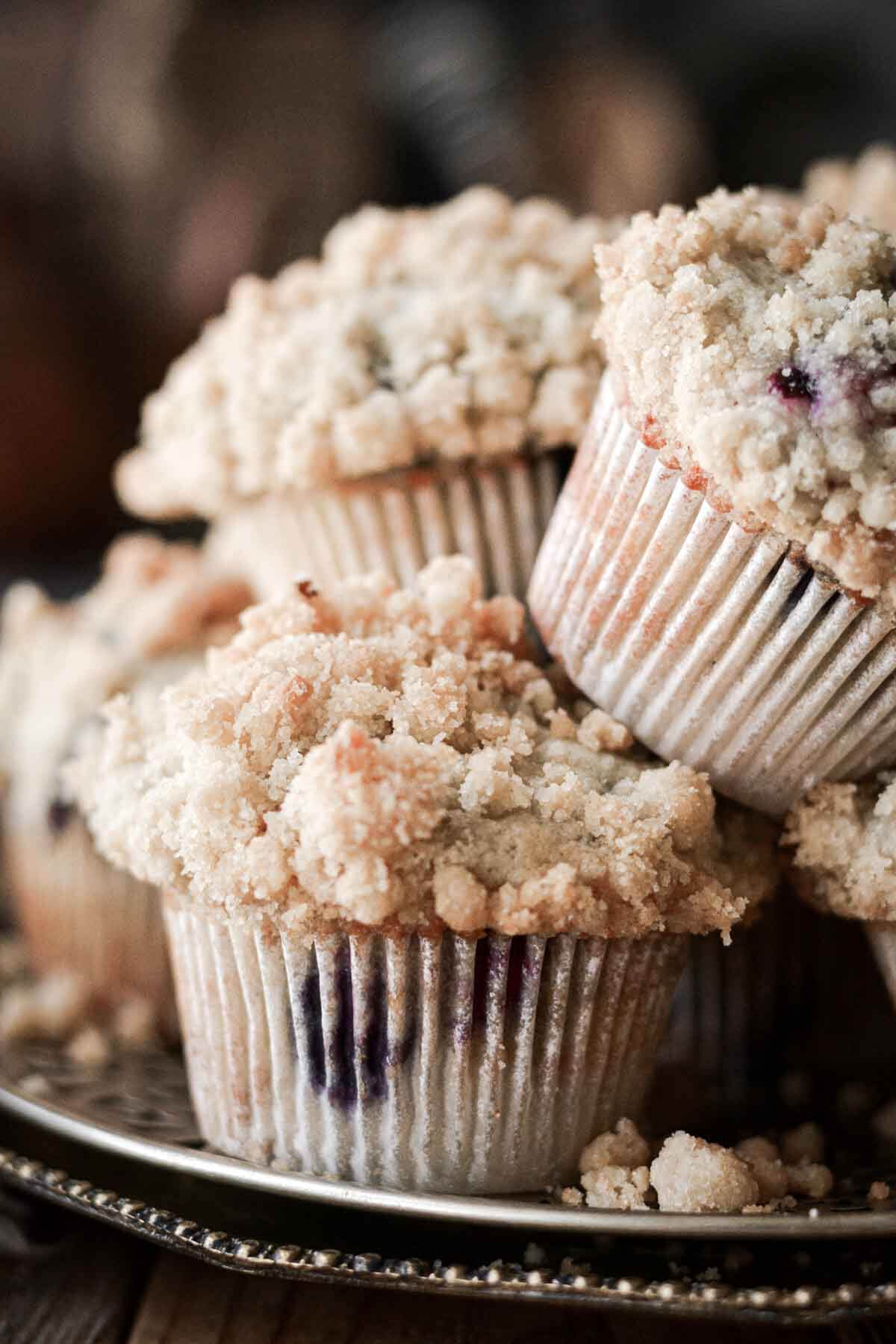 Blueberry crumb muffins stacked on a plate.