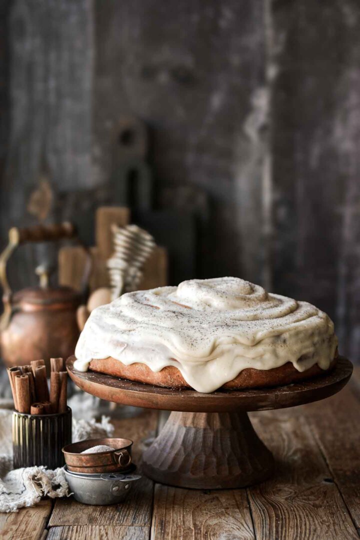 Giant cinnamon roll cake with cream cheese frosting on a wooden cake stand.
