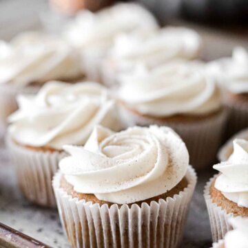 Carrot cake cupcakes with piped swirls of cream cheese buttercream and cinnamon sugar sprinkled on top.