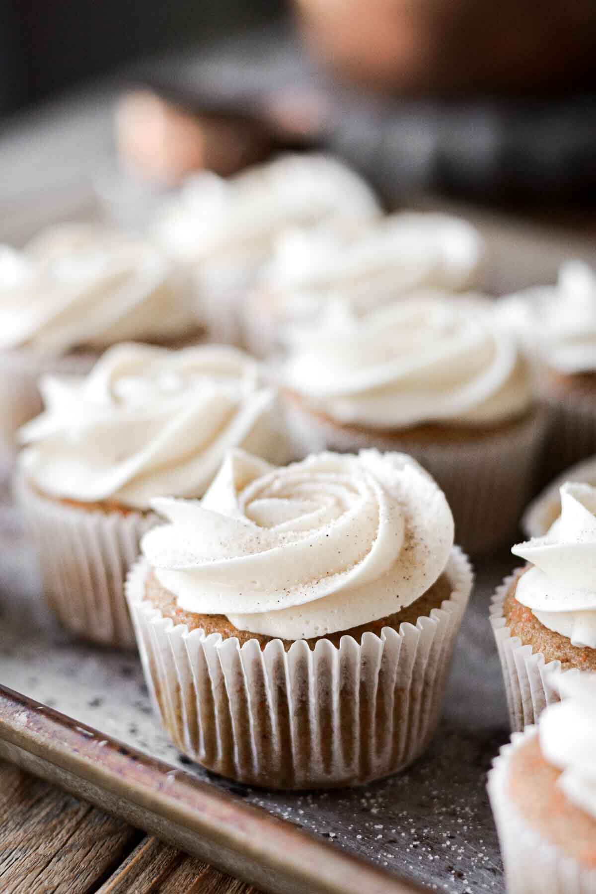 Carrot cake cupcakes with piped swirls of cream cheese buttercream and cinnamon sugar sprinkled on top.