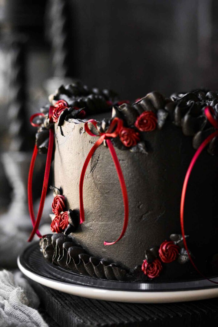 A gothic cake decorated with red ribbons and black cocoa buttercream.