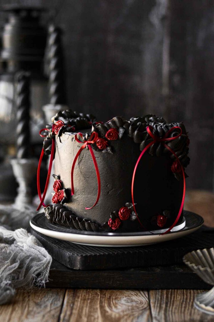 A gothic red velvet chocolate chip cake for Halloween, with black cocoa buttercream and red ribbons.