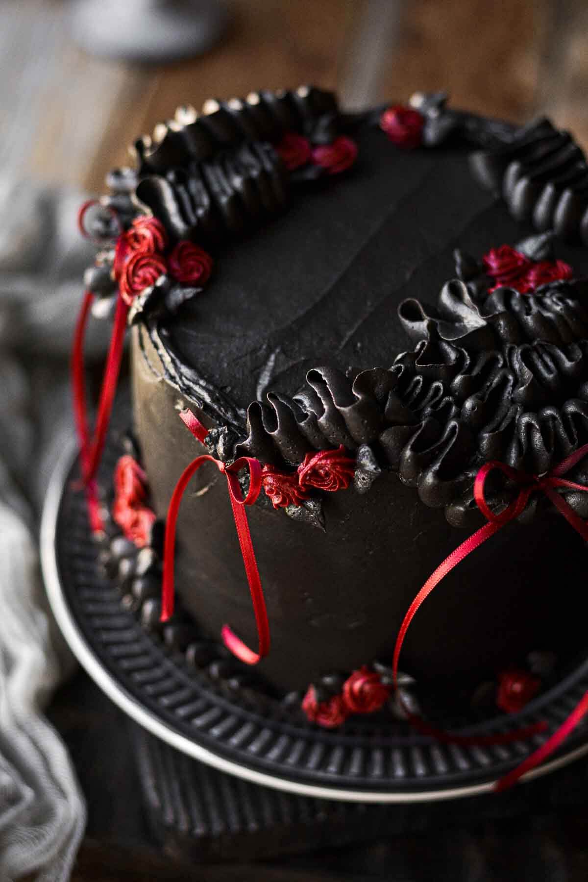 A gothic red velvet chocolate chip cake for Halloween, with black cocoa buttercream and red ribbons.