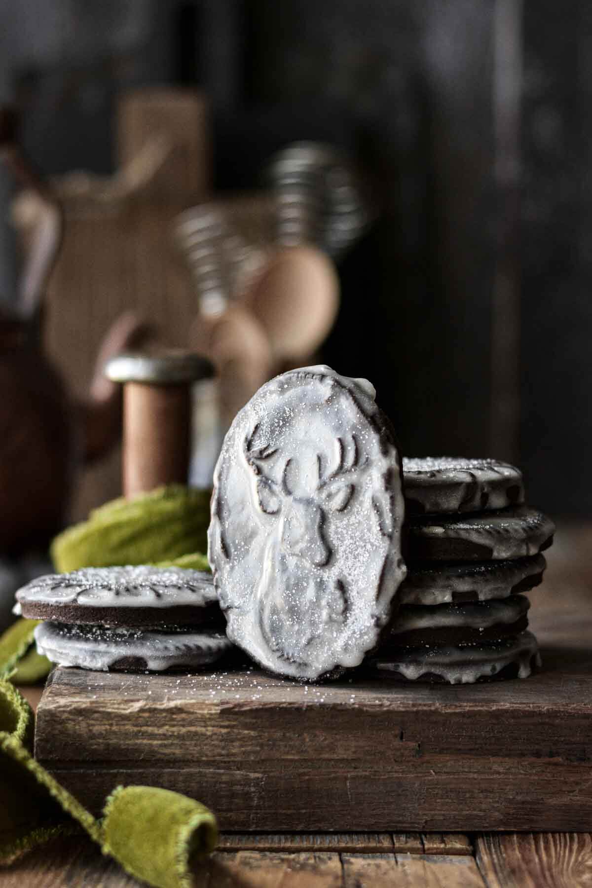 An iced reindeer cookie, leaning against a stack of cookies.